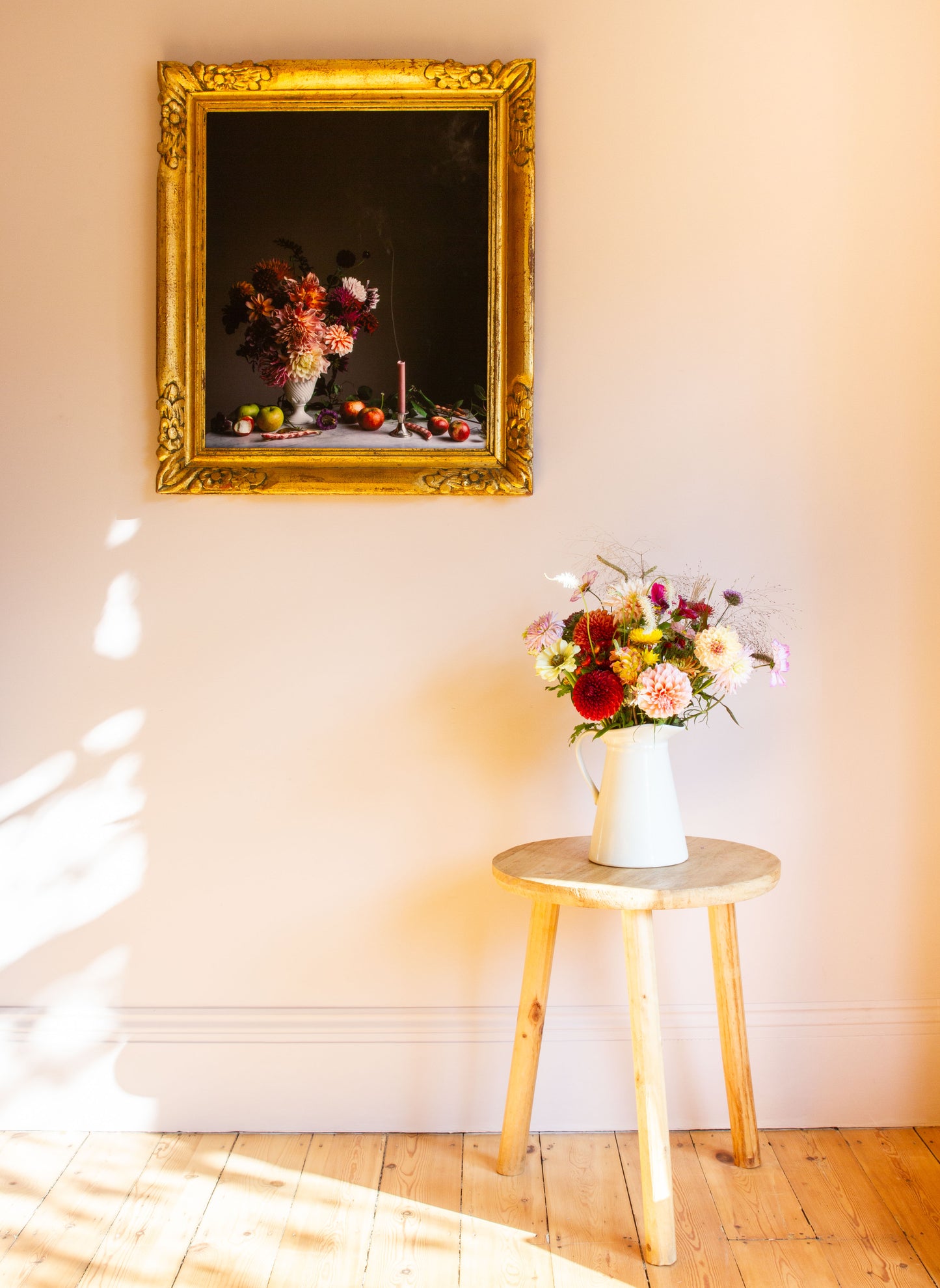Decorative still life floral photograph on a wall with a vase of flowers on a stool below.