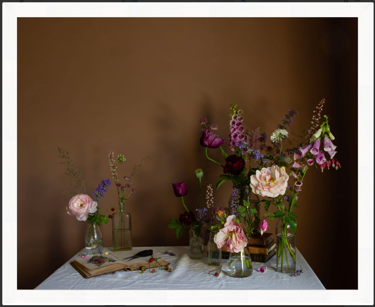 Framed photographic still life image showing an arrangement of flowers in vases on a table with a brown background
