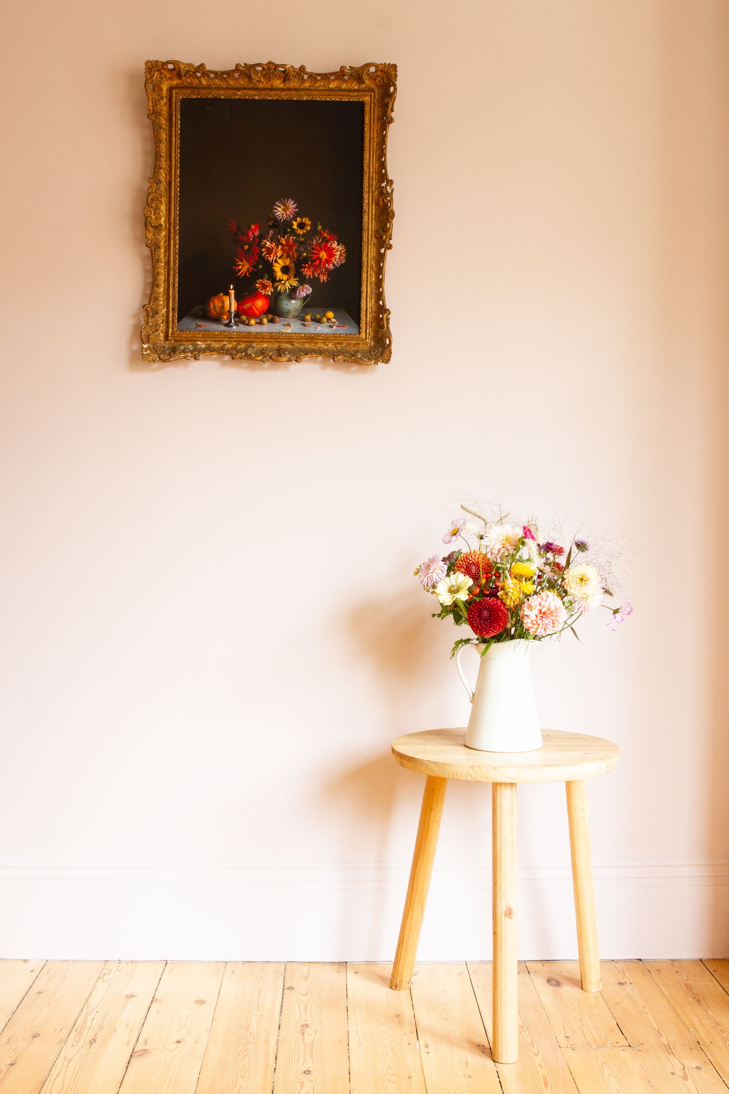 Floral arrangement on a stool with a framed still-life picture of flowers on the wall.