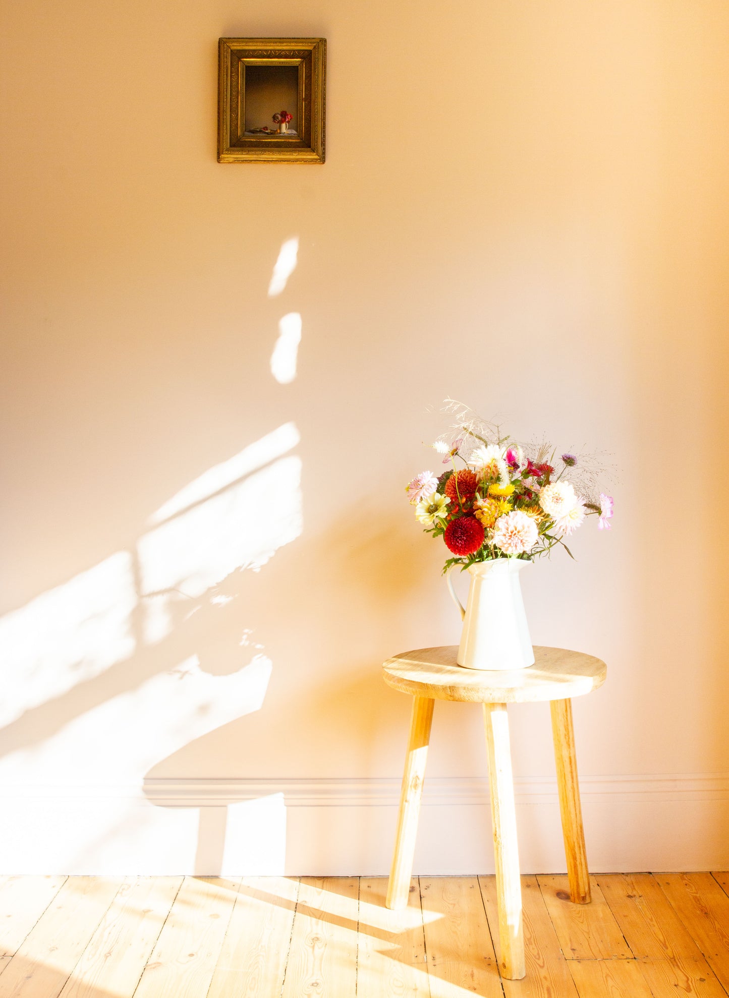 Floral arrangement on a small table with sunlight casting shadows on a wall, alongside a floral still-life photograph