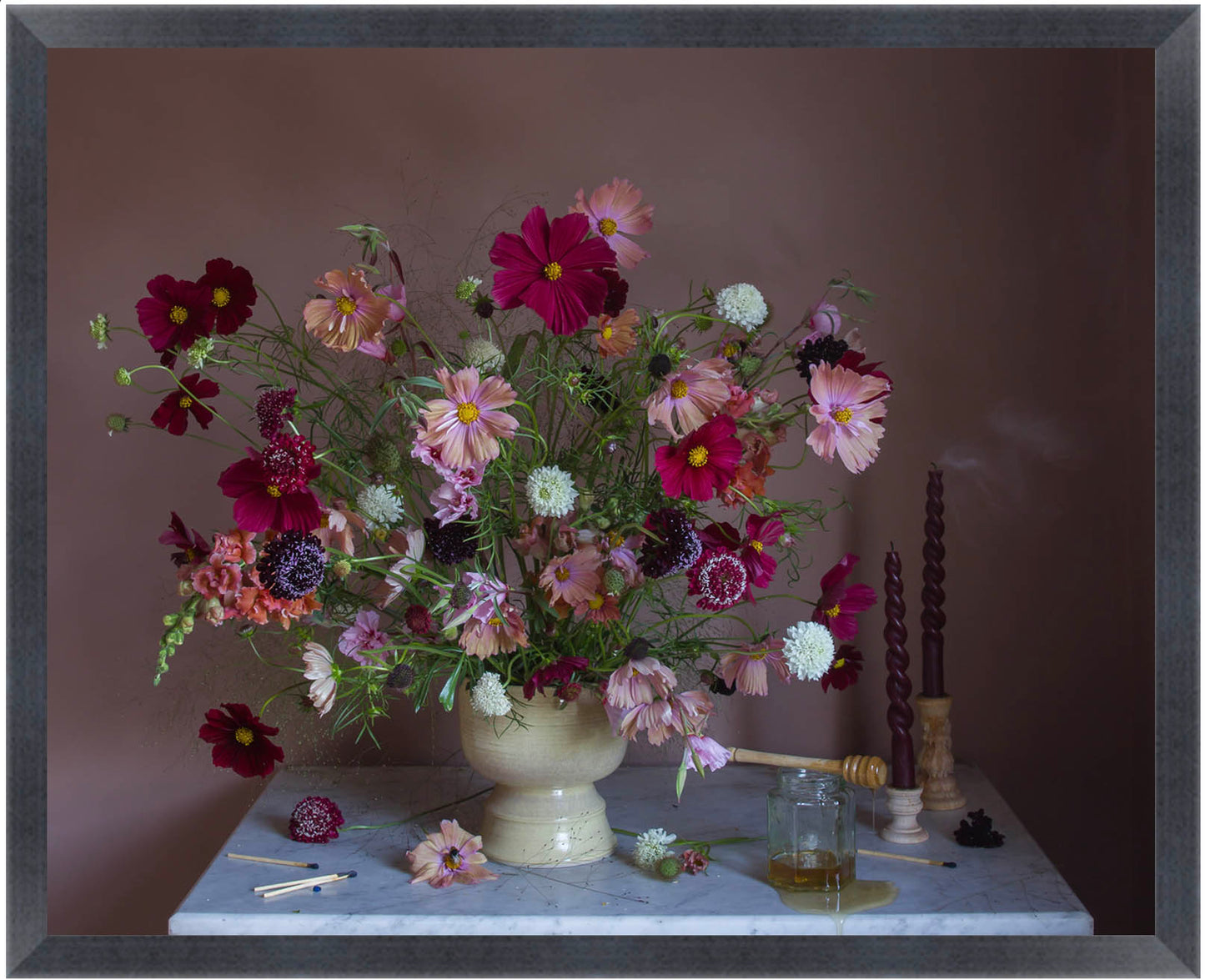 Framed photograph of a bouquet of flowers in a vase on a marble surface with candles and a glass container.