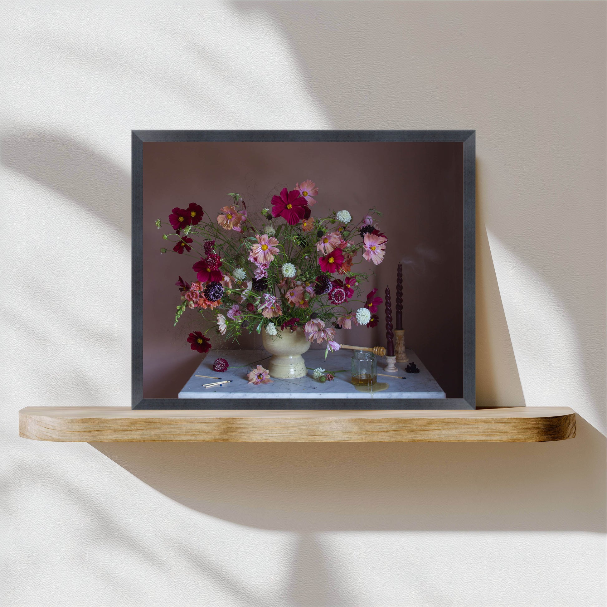 Framed photograph of a floral arrangement on a wooden shelf with a neutral background