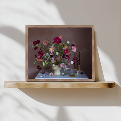 Framed still life photograph with flowers on a wooden shelf against a neutral background