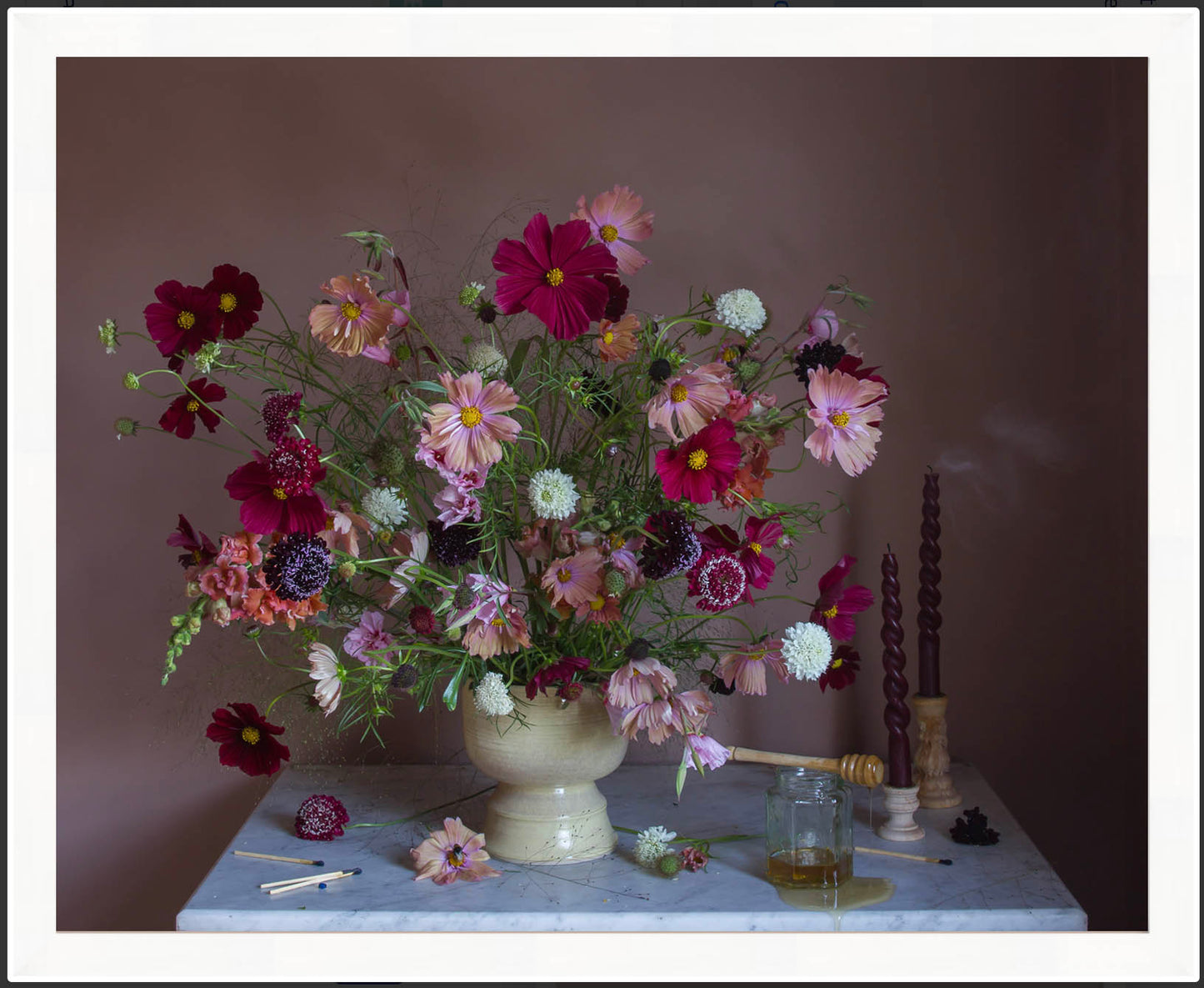 Still-life of flowers in a vase on a table with candles and a glass container against a dark background