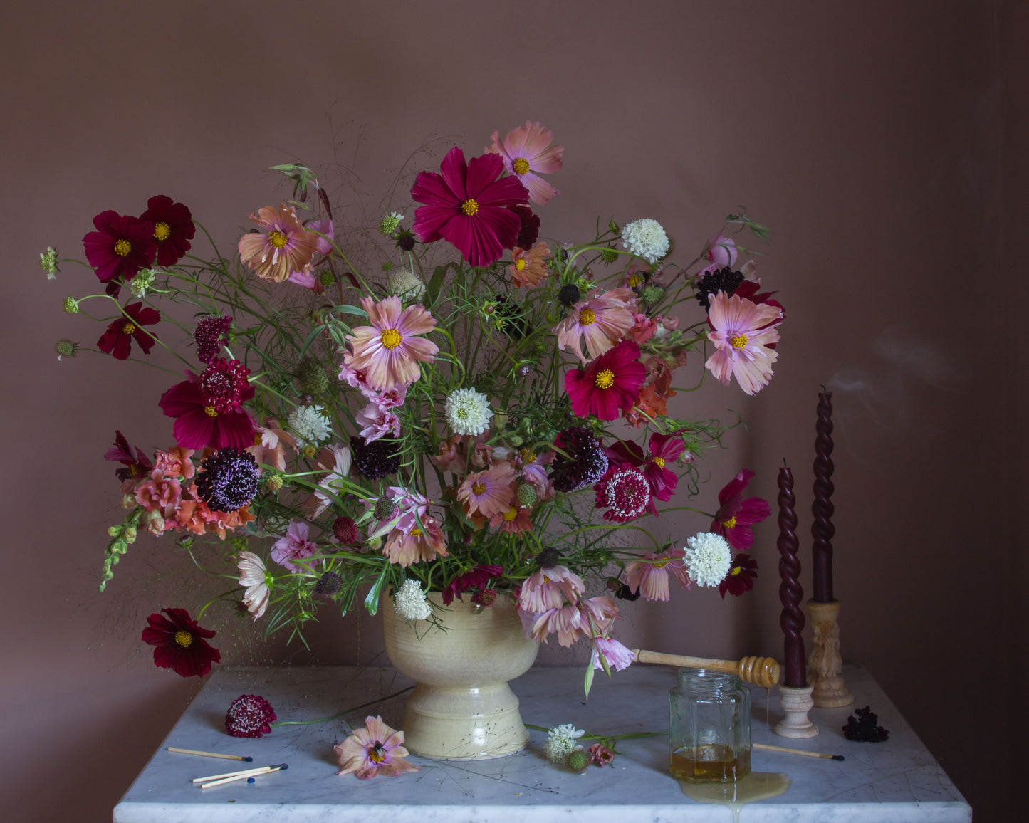 Limited edition fine art photograph by Emma Harris of a bouquet of cosmos flowers in a vase on a marble surface with candles and a jar.