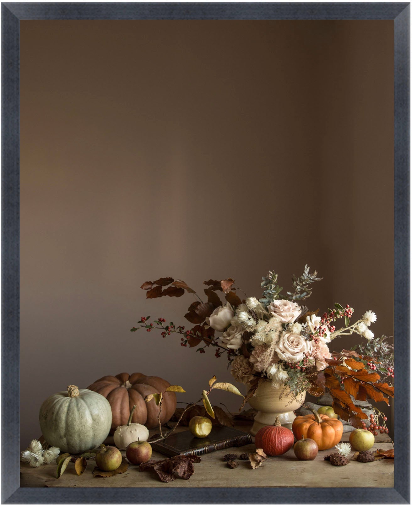 framed Still life flower art with pumpkins, apples, and flowers on a wooden surface against a brown background.