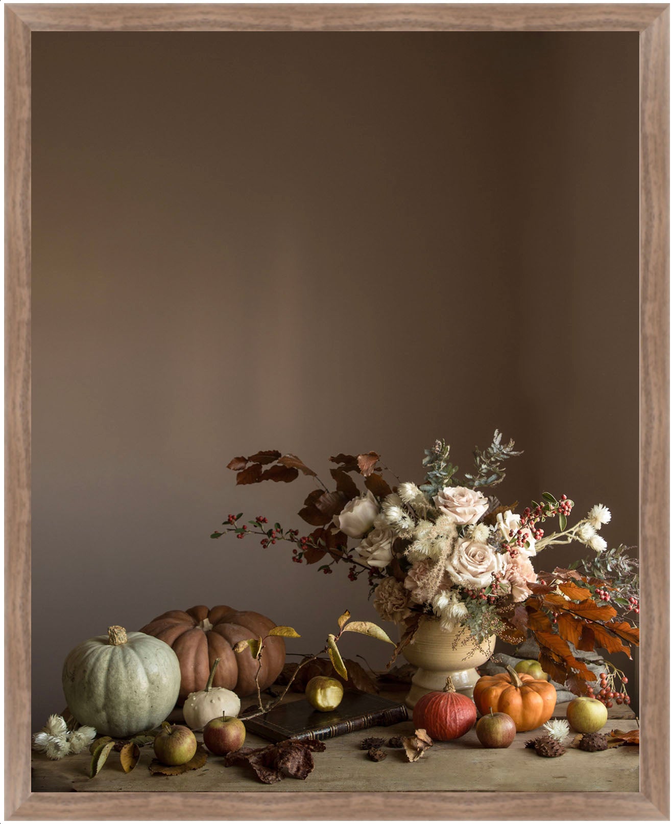 Framed floral art with pumpkins and flowers on a wooden surface against a brown background