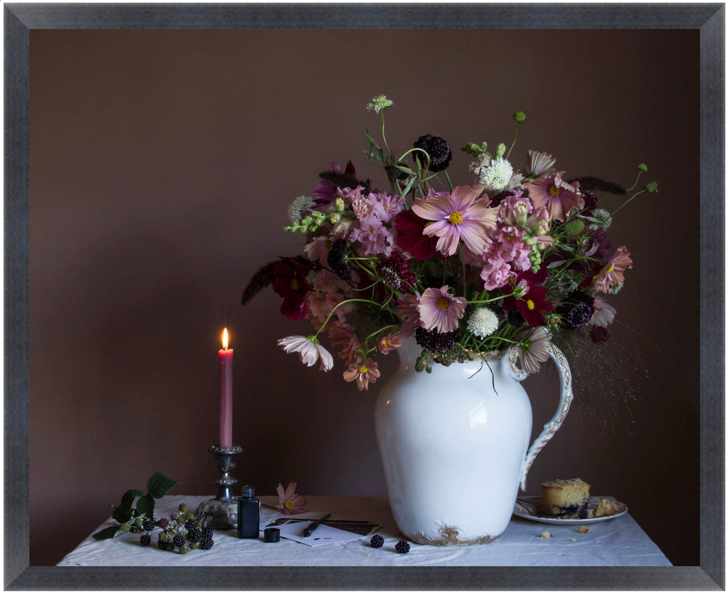 Framed still life arrangement with flowers in a white vase, candle, and small plate on a table against a dark background.