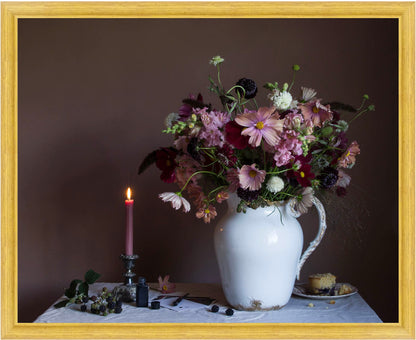 Framed still-life of a floral arrangement in a white vase with a lit candle and small plate on a table against a dark background.