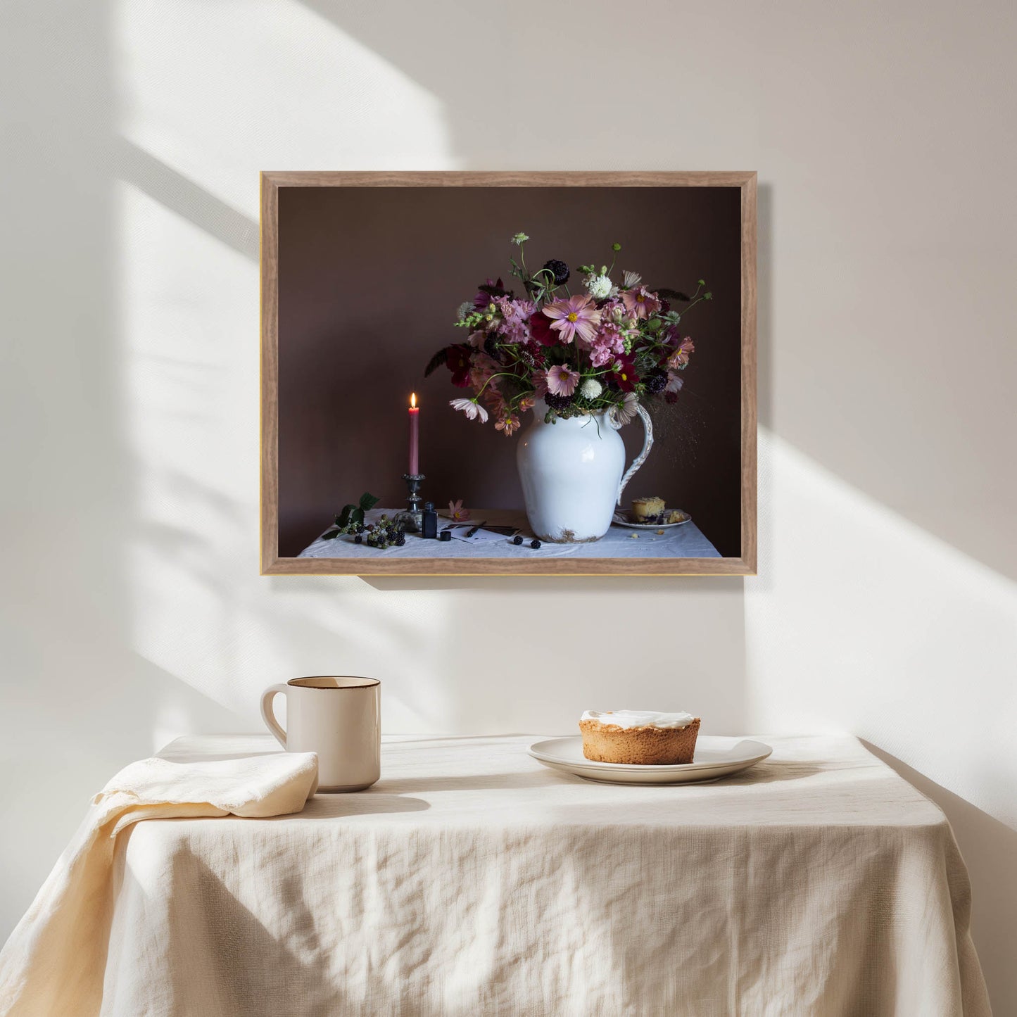 Framed artwork of a floral arrangement on a wall above a table with a pie and mug.