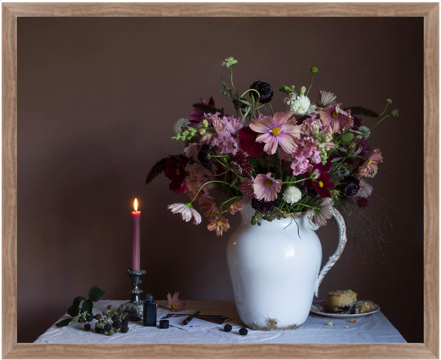 Fine art photograph by Emma Harris showing a floral arrangement in a white pitcher with a lit candle and small plate on a dark background
