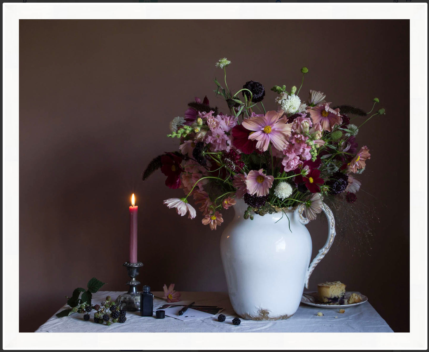 Framed fine art photograph of a foral arrangement in a white pitcher with a lit candle on a dark background