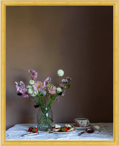 Framed still life scene with flowers in a vase, a cup, and a plate on a table against a dark background.