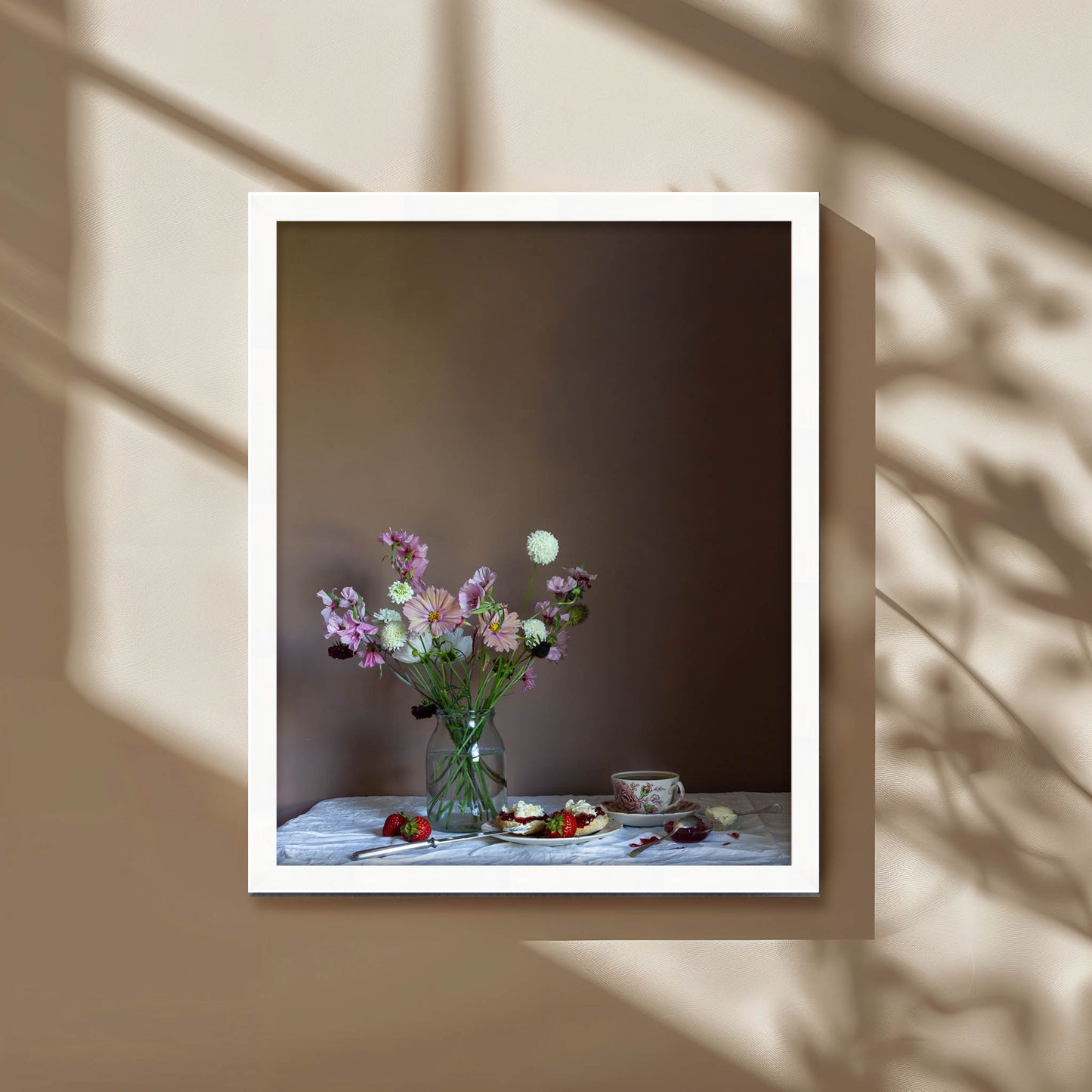 Framed photograph of a still life scene with flowers and food on a table against a brown background.