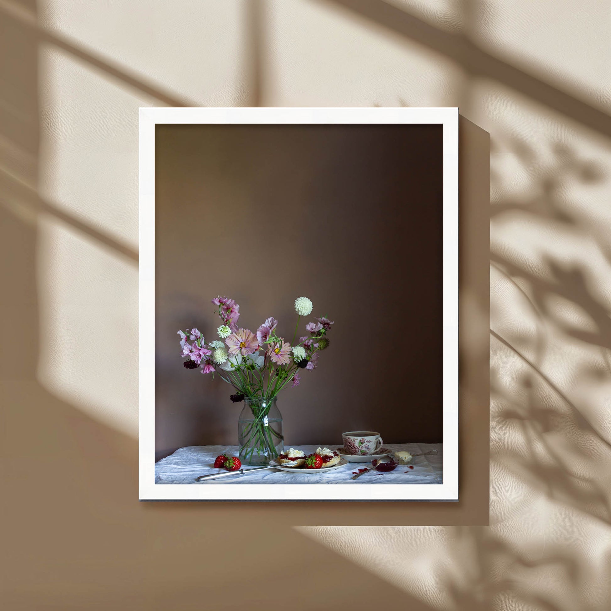 Framed photograph of a still life scene with flowers and food on a table against a brown background.