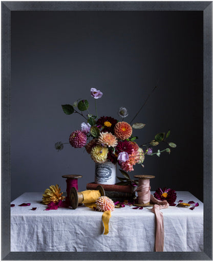 Still life arrangement with flowers, ribbons, and spools on a tablecloth against a dark background.   Botanical artwork