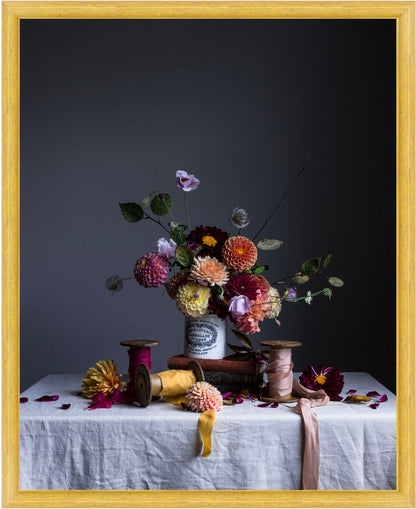 Still life arrangement with flowers and spools on a table against a dark background.   floral artwork