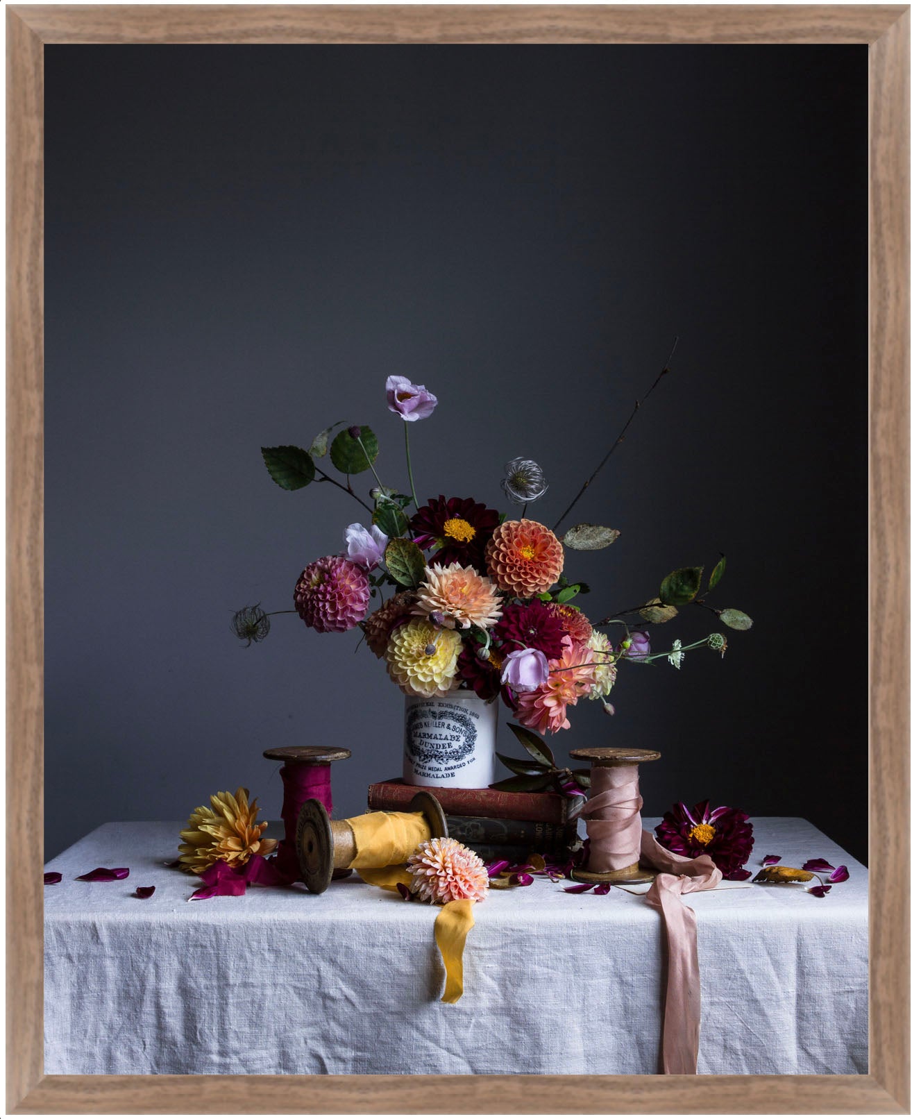Still life arrangement with flowers, spools of thread, and ribbons on a tablecloth against a dark background.   Floral art