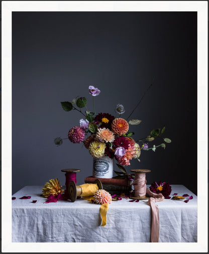 Floral arrangement in a vase on a table with spools of thread against a dark background.   Flower art