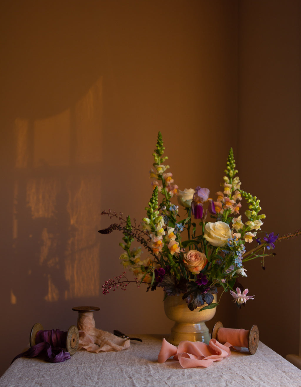 A fine art floral photograph featuring a vase of multicolored flowers, placed on a table with a backdrop of a warm-toned wall by photographer Emma Harris