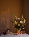 A fine art floral photograph featuring a vase of multicolored flowers, placed on a table with a backdrop of a warm-toned wall by photographer Emma Harris