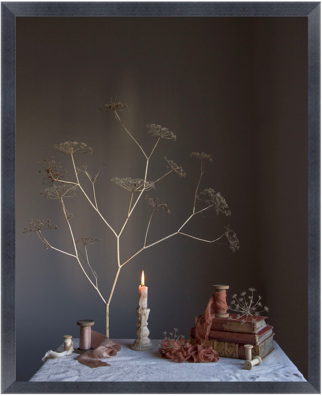 Still life arrangement with dried plants, books, and a candle on a dark background.   Floral print.