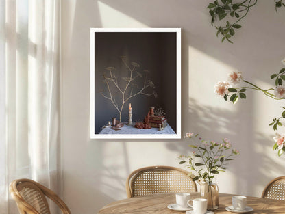 Framed artwork on a wall with a table and chairs in the foreground.  Floral still-life