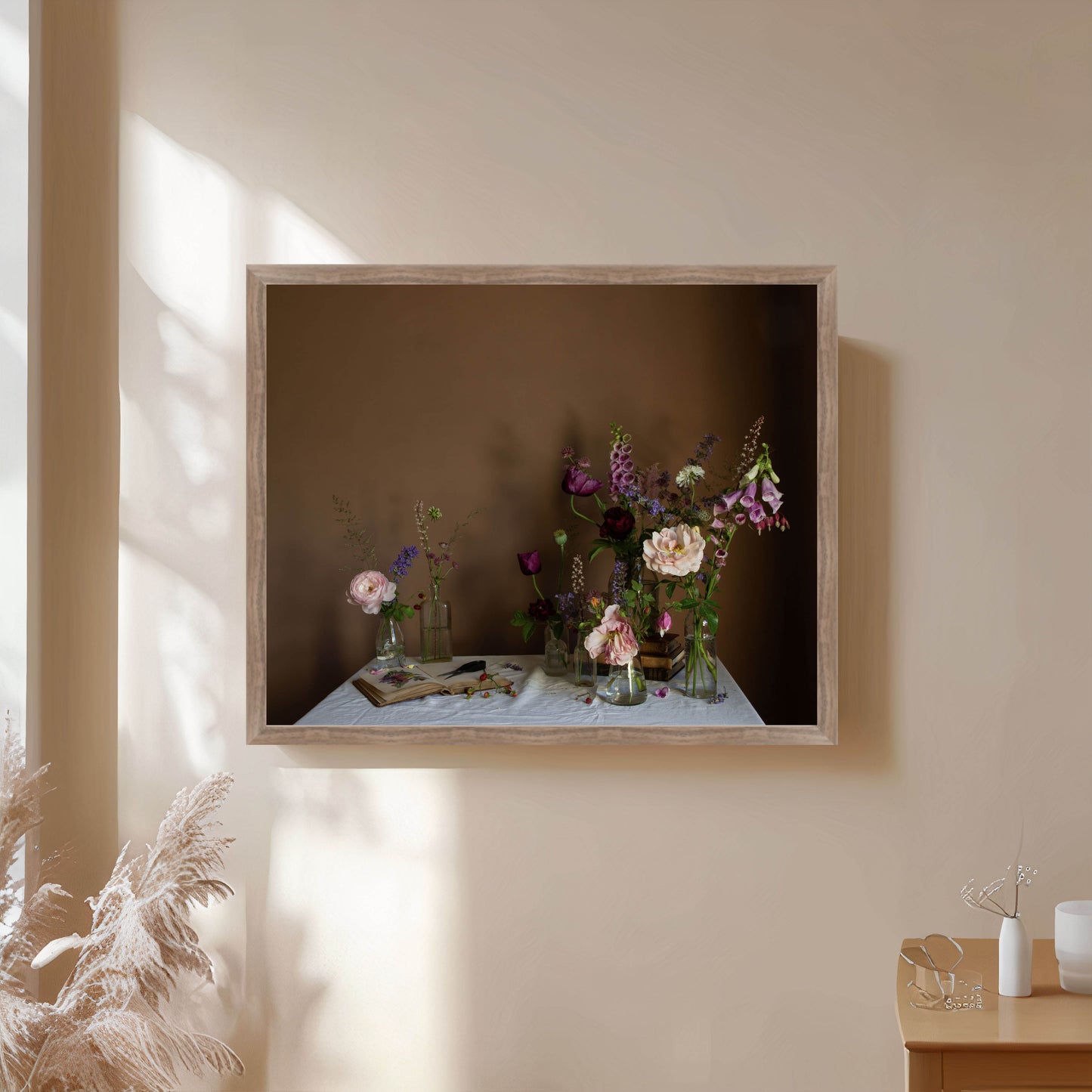Framed still-life photograph of flowers on a table against a beige wall.