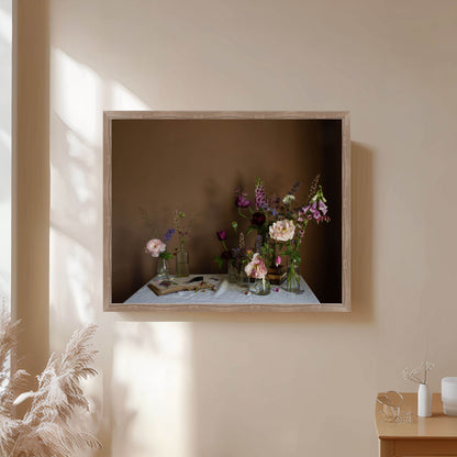 Framed still-life photograph of flowers on a table against a beige wall.