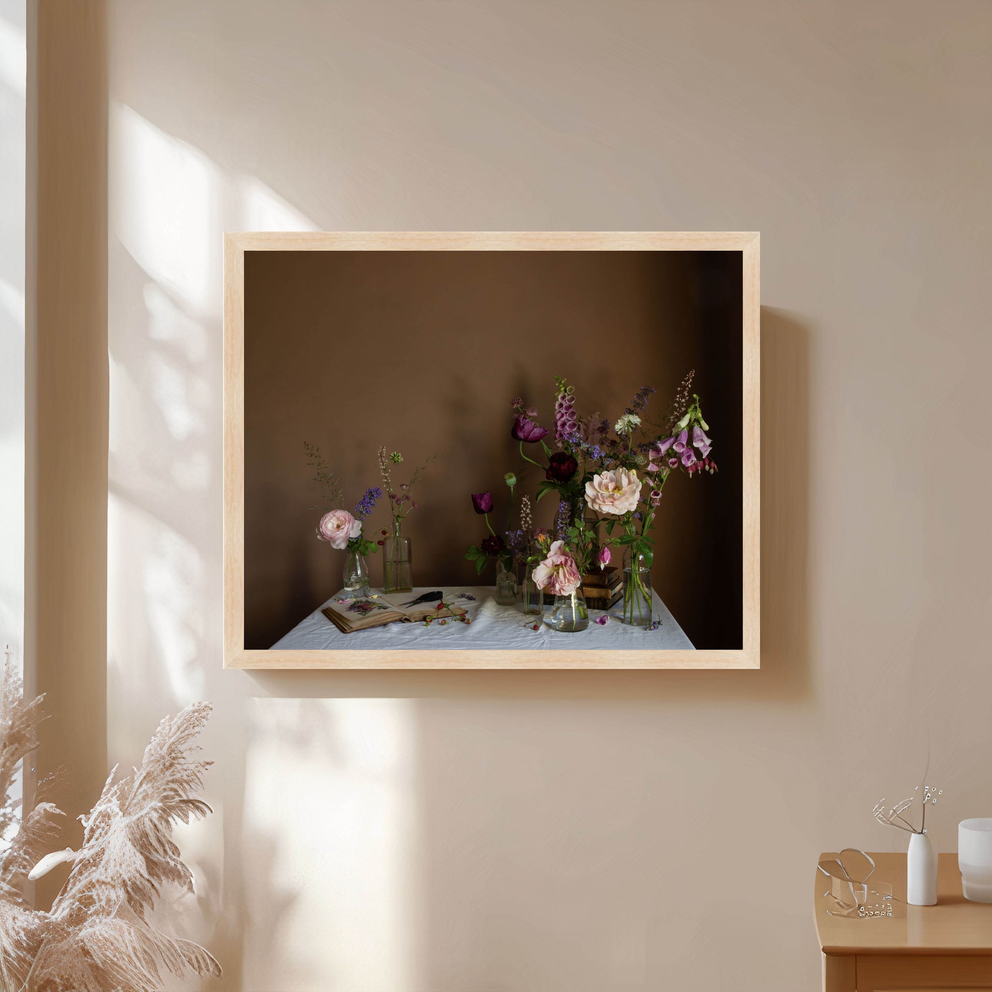 Framed artwork of a still life with flowers on a table against a plain wall.