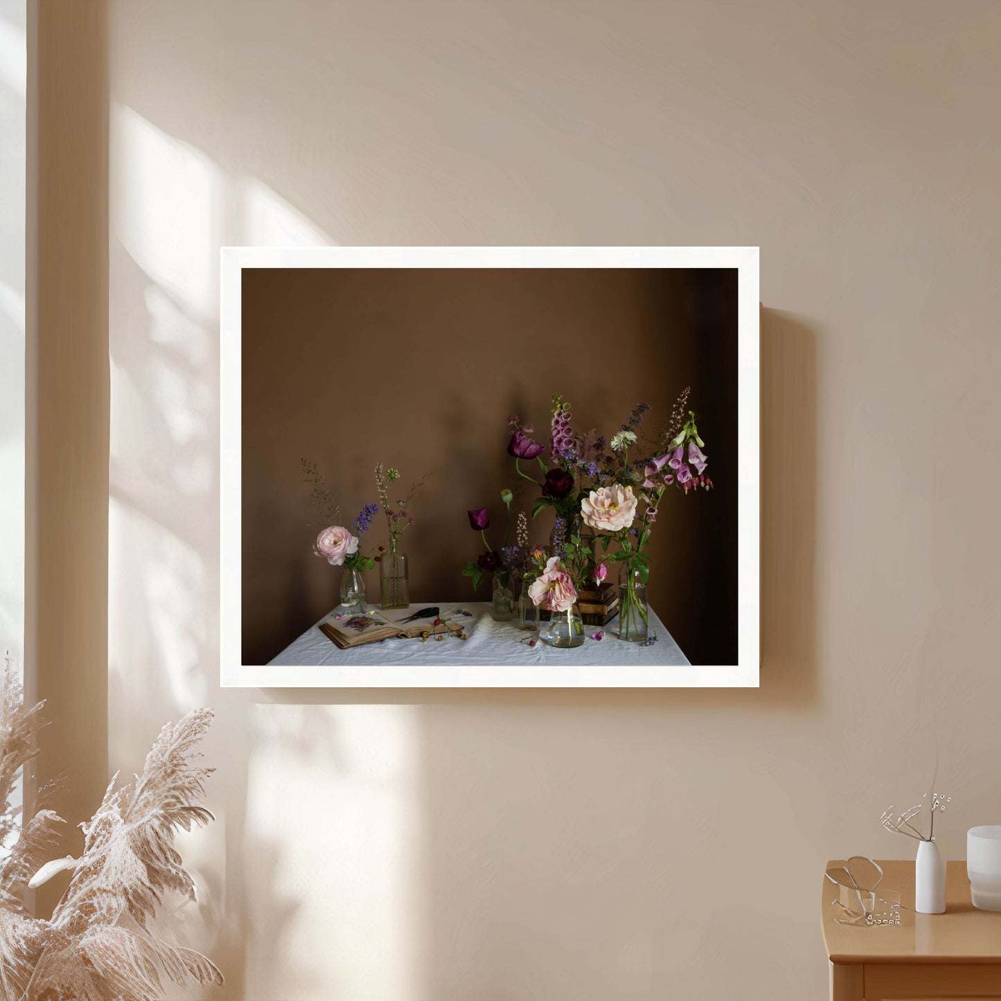 Framed photograph of a table with flowers and books on a beige wall.