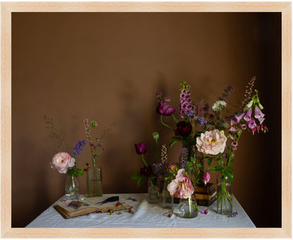 Framed still life arrangement with flowers in vases on a table against a brown background