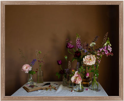 Framed still life arrangement with flowers and books on a table against a brown background