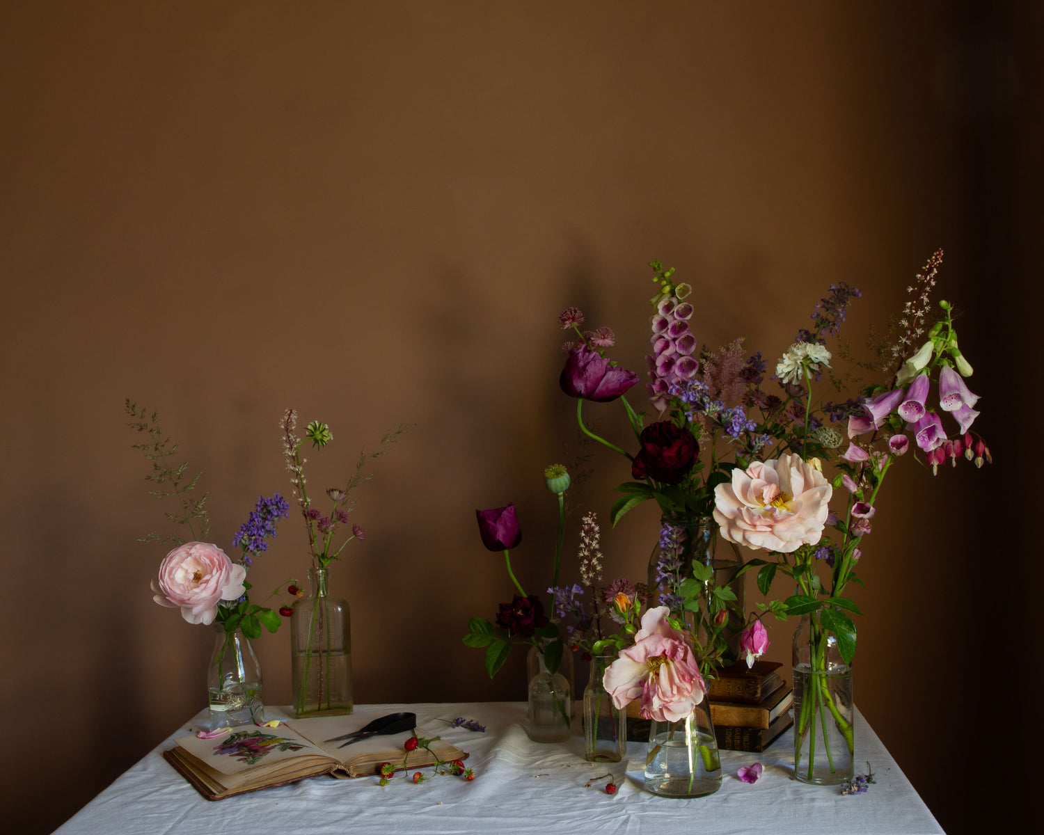 Photographic print of an arrangement of flowers in vases on a table with a brown background by Emma Harris
