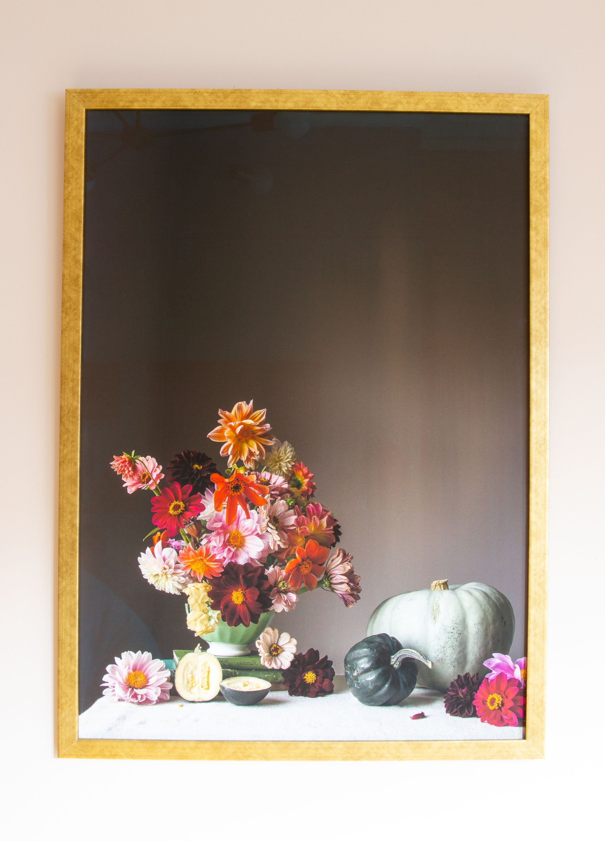 Framed artwork of a still life with flowers and pumpkins on a table.