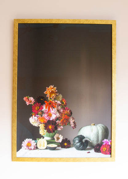 Framed artwork of a still life with flowers and pumpkins on a table.