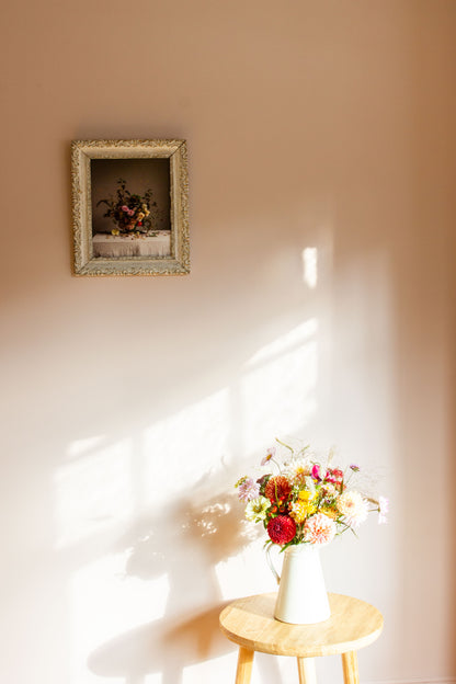 Floral arrangement on a small table with a framed floral still-life on the wall in the background.