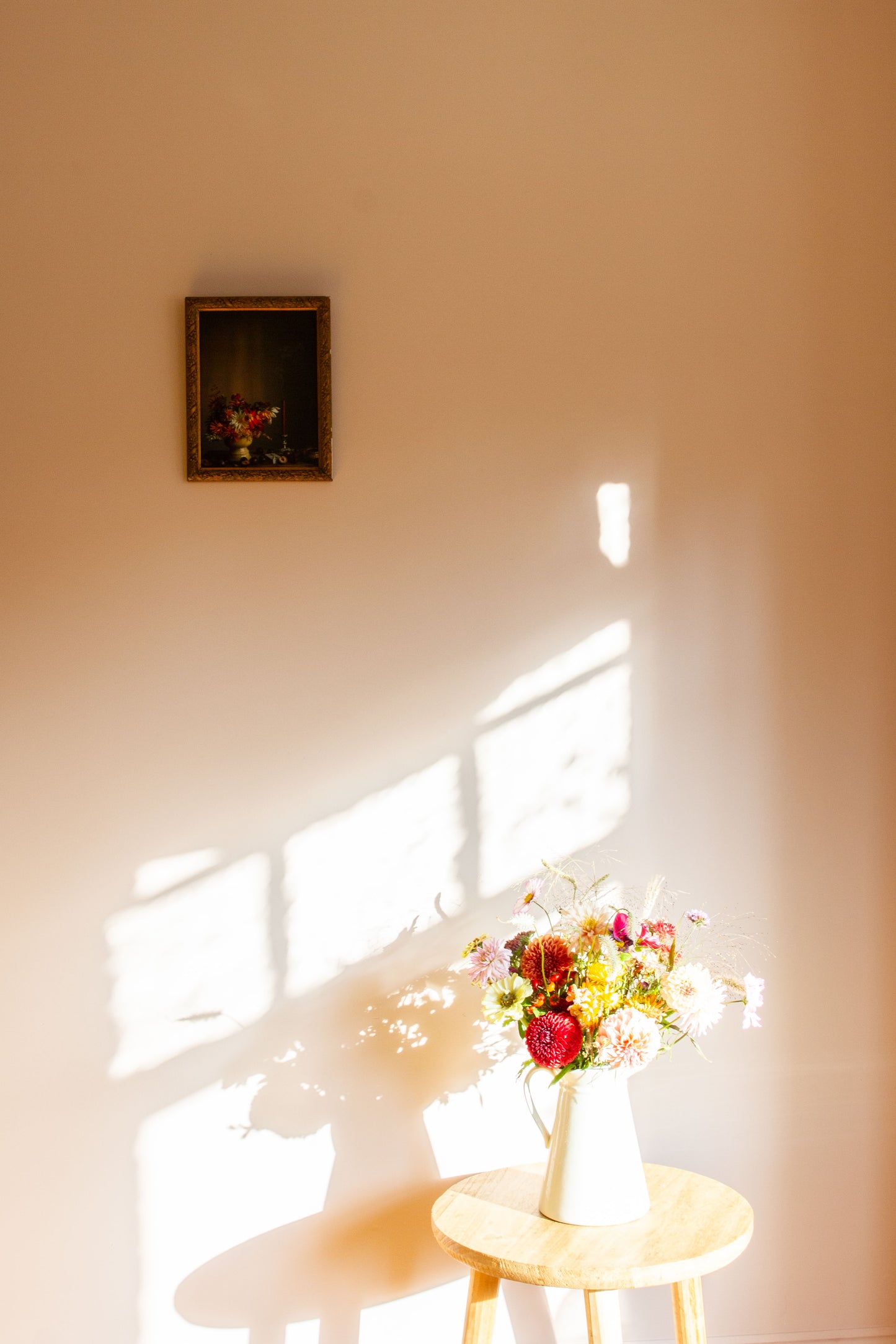 Bouquet of flowers on a small table with a framed still-life picture on the wall.