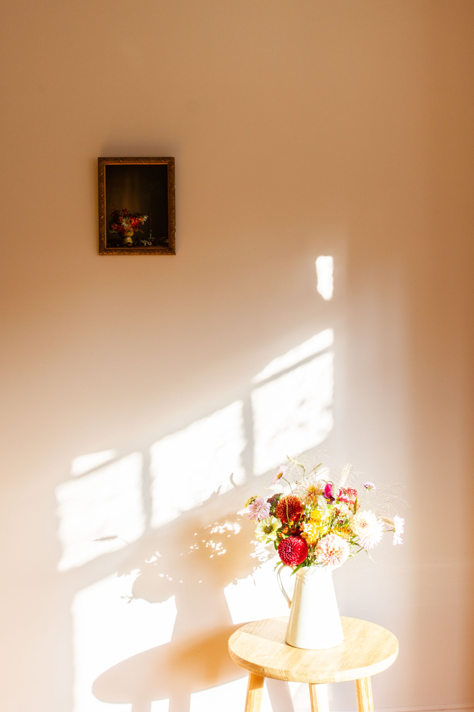 Bouquet of flowers on a small table with a framed still-life picture on the wall.