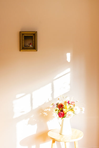 Floral arrangement on a small table with a gold-framed still-life picture on the wall.
