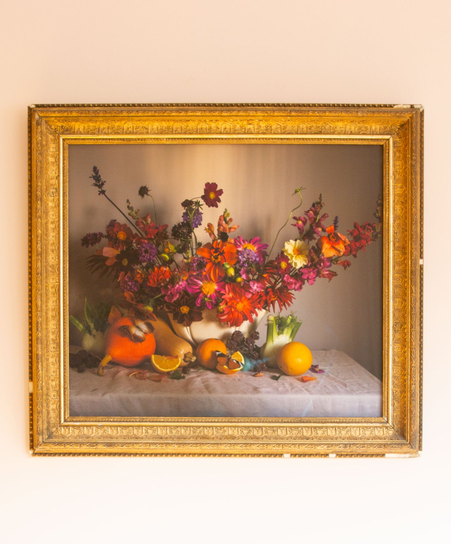 Framed still life picture with flowers and fruits on a beige wall