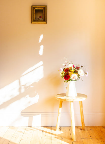 Floral arrangement on a small table with sunlight casting shadows on a wall, alongside a floral still-life photograph