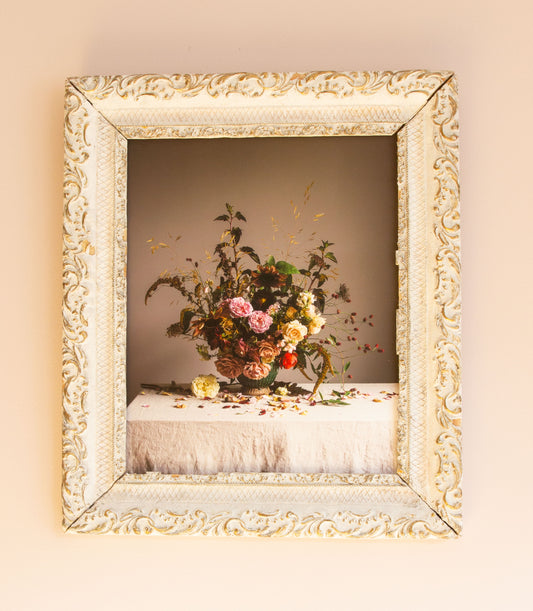 Decorative still-life floral arrangement in a ornate gold frame on a pink wall.