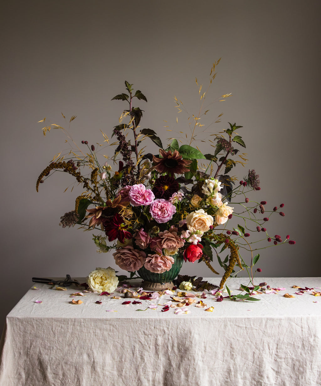 Botanical still-life by Emma Harris containing a floral arrangement with various dried flowers such as violas and grasses, placed on a linen surface with a grey background.