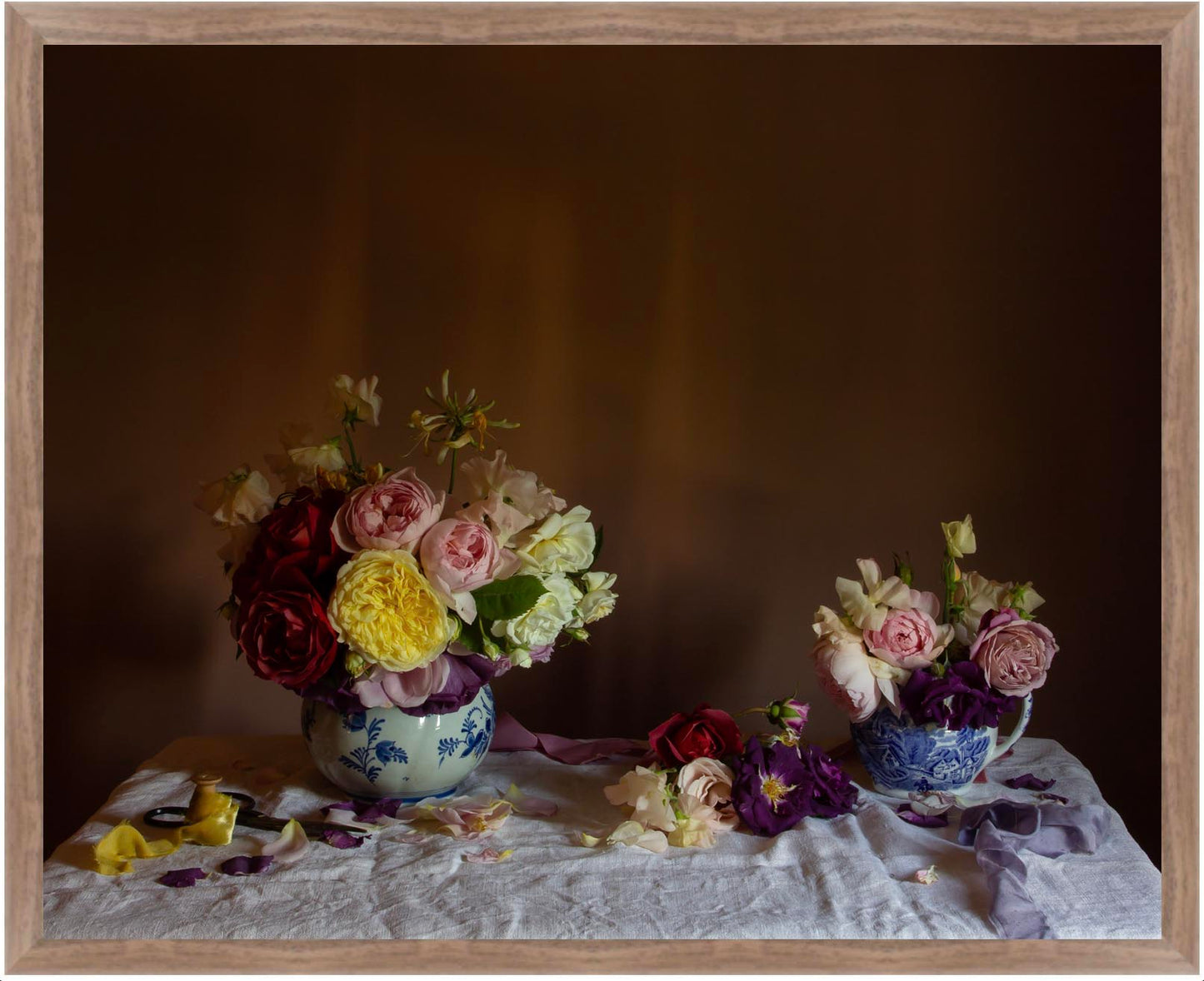 Floral still-life showing two floral arrangements of roses in jugs on a tablecloth with a dark background in a walnut frame