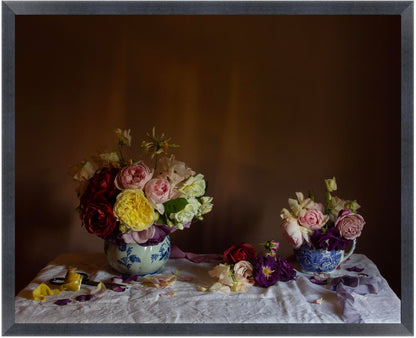 Floral still-life art print in black frame showing floral arrangements of roses in jugs on a tablecloth with a dark background