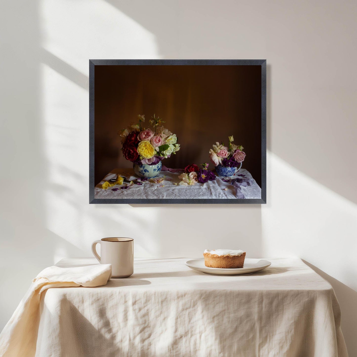 Framed floral still-life artwork of flowers on a table with a pie and cup, sunlight casting shadows.