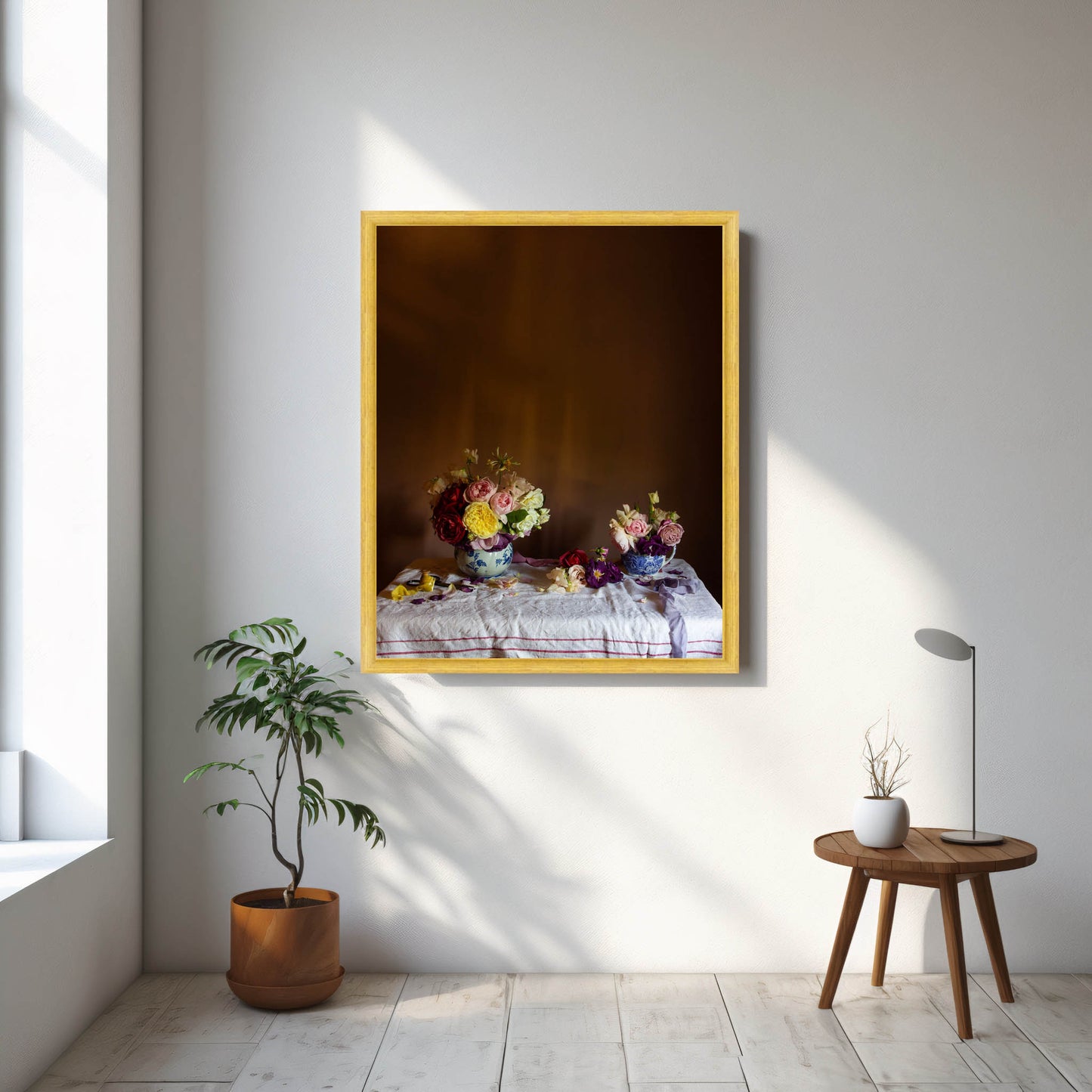 Framed floral artwork on a wall with a plant and small table in the foreground