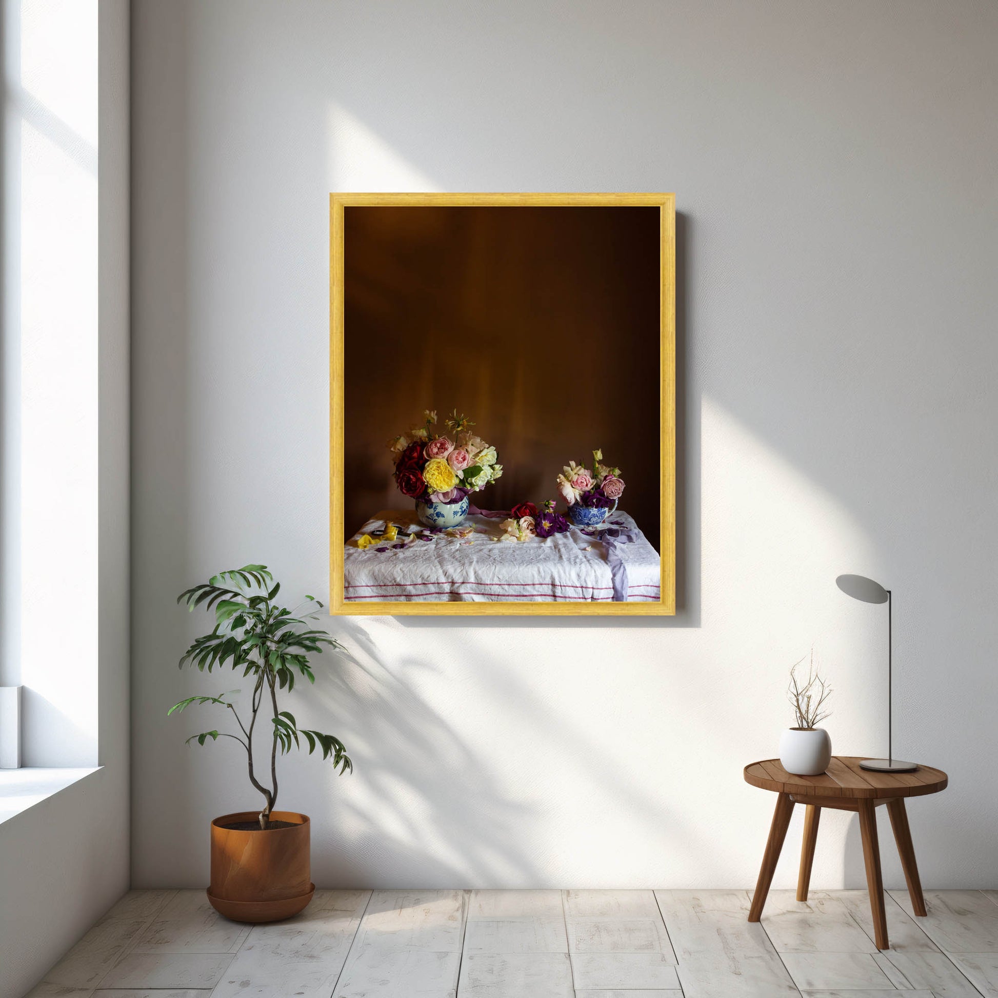 Framed floral artwork on a wall with a plant and small table in the foreground