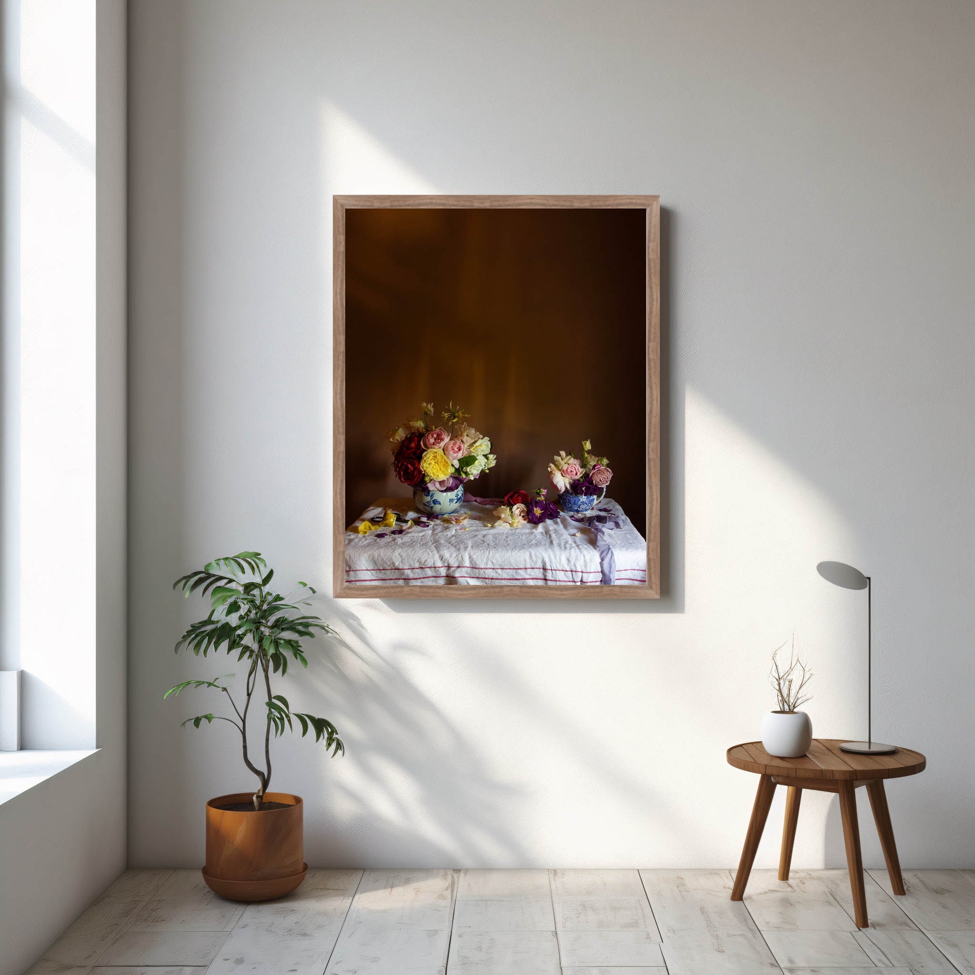 Framed artwork on a wall with a plant and small table in a room.
